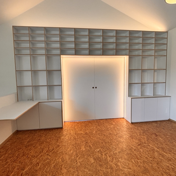 Weißes Einbauregal mit Schreibtisch und geschlossener Schiebetür mit umlaufender warmer LED-Beleuchtung